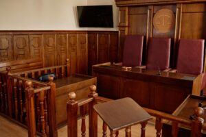 Corner of courtroom with wooden desks and railings and leather chairs