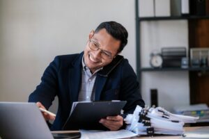 Portrait of young asian businessman, man smiling while sitting inside office, boss in business suit