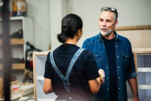 Senior caucasian man working with asian woman partner in small business wood workshop