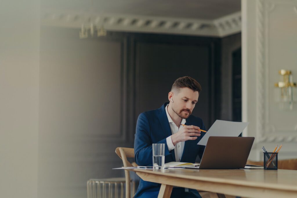 Thinking business executive sitting at his desk in front of laptop and analyzing documents